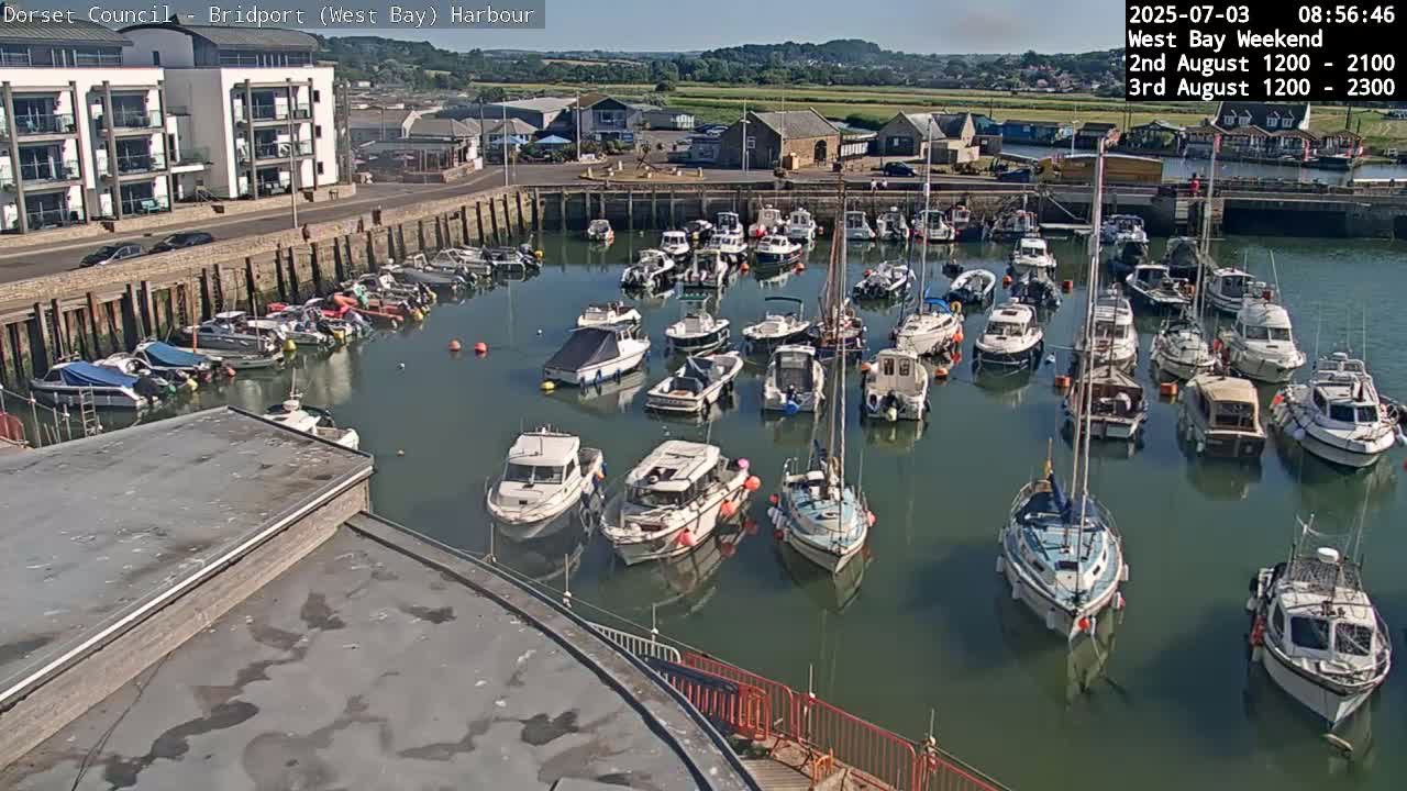 Many boats are moored in a calm harbor on a sunny day.