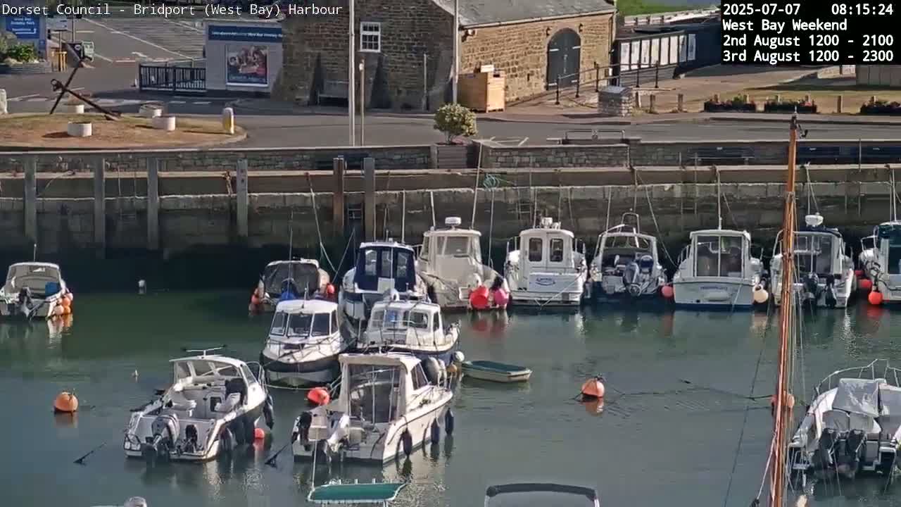 Several motorboats are moored alongside a harbor wall on a sunny day.