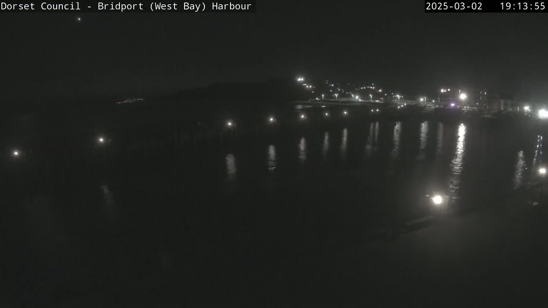 A nighttime view of a calm harbor with lights reflecting on the water.