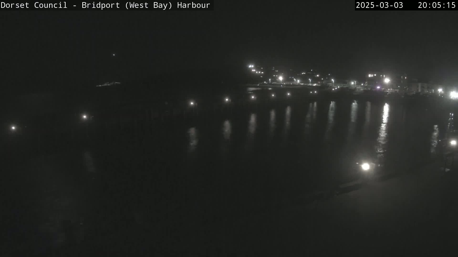 A nighttime view of a calm harbor with lights reflecting on the water.