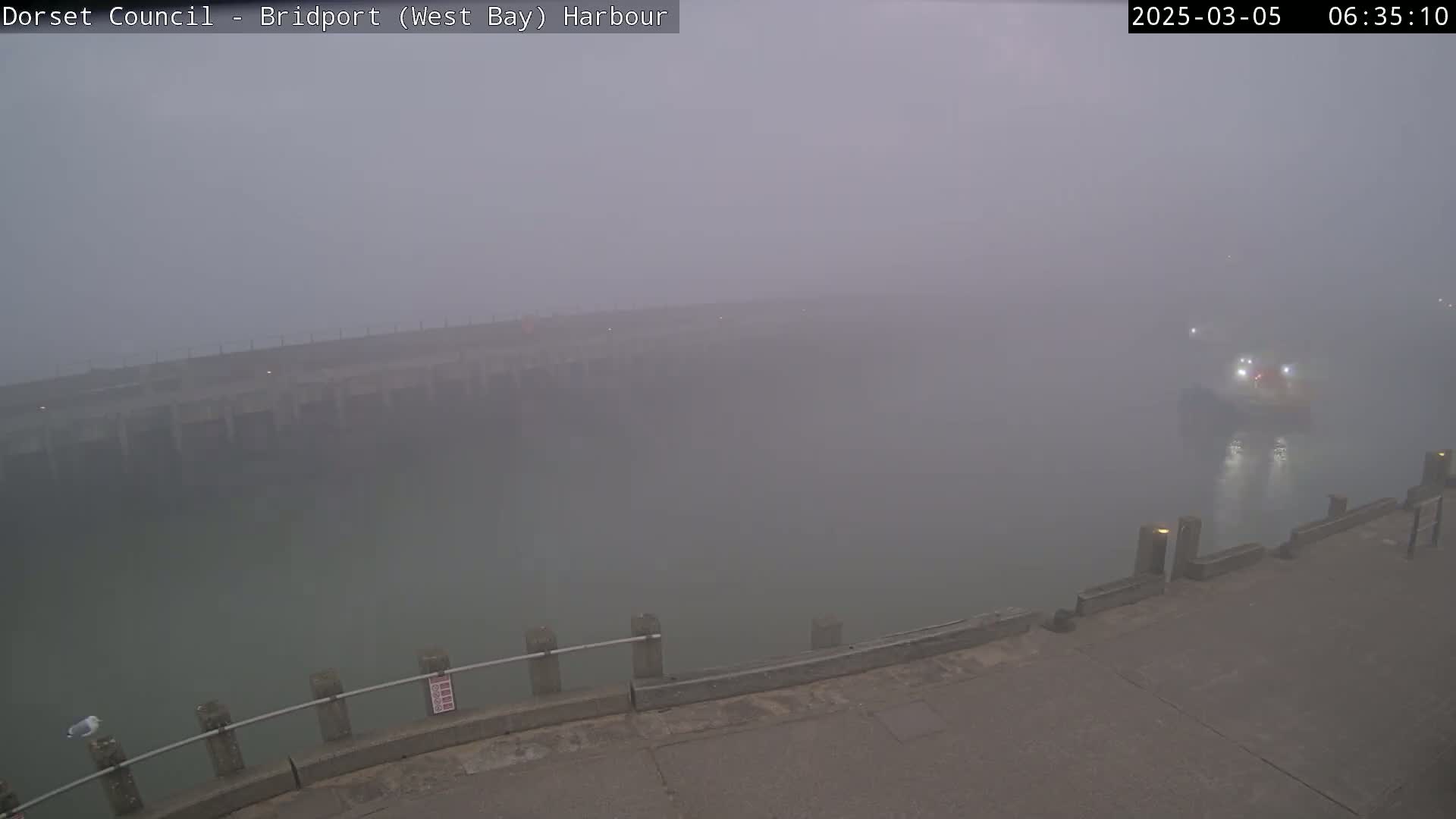 A harbor shrouded in thick fog, with a small vessel visible in the distance.