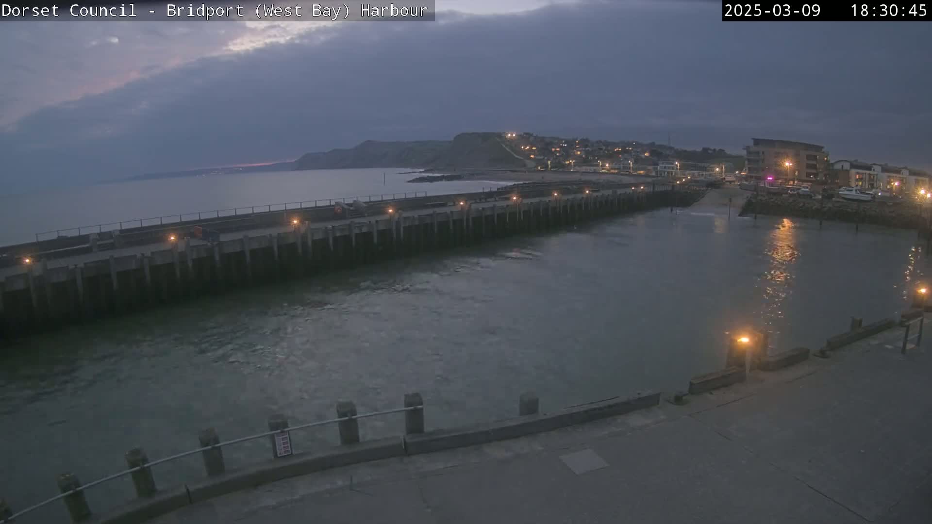 A harbor at twilight, with calm water reflecting lights from the harbor walls and nearby buildings.