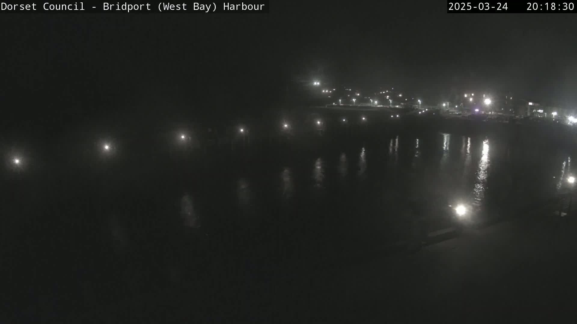 A nighttime view of a calm harbor with lights reflecting on the water.