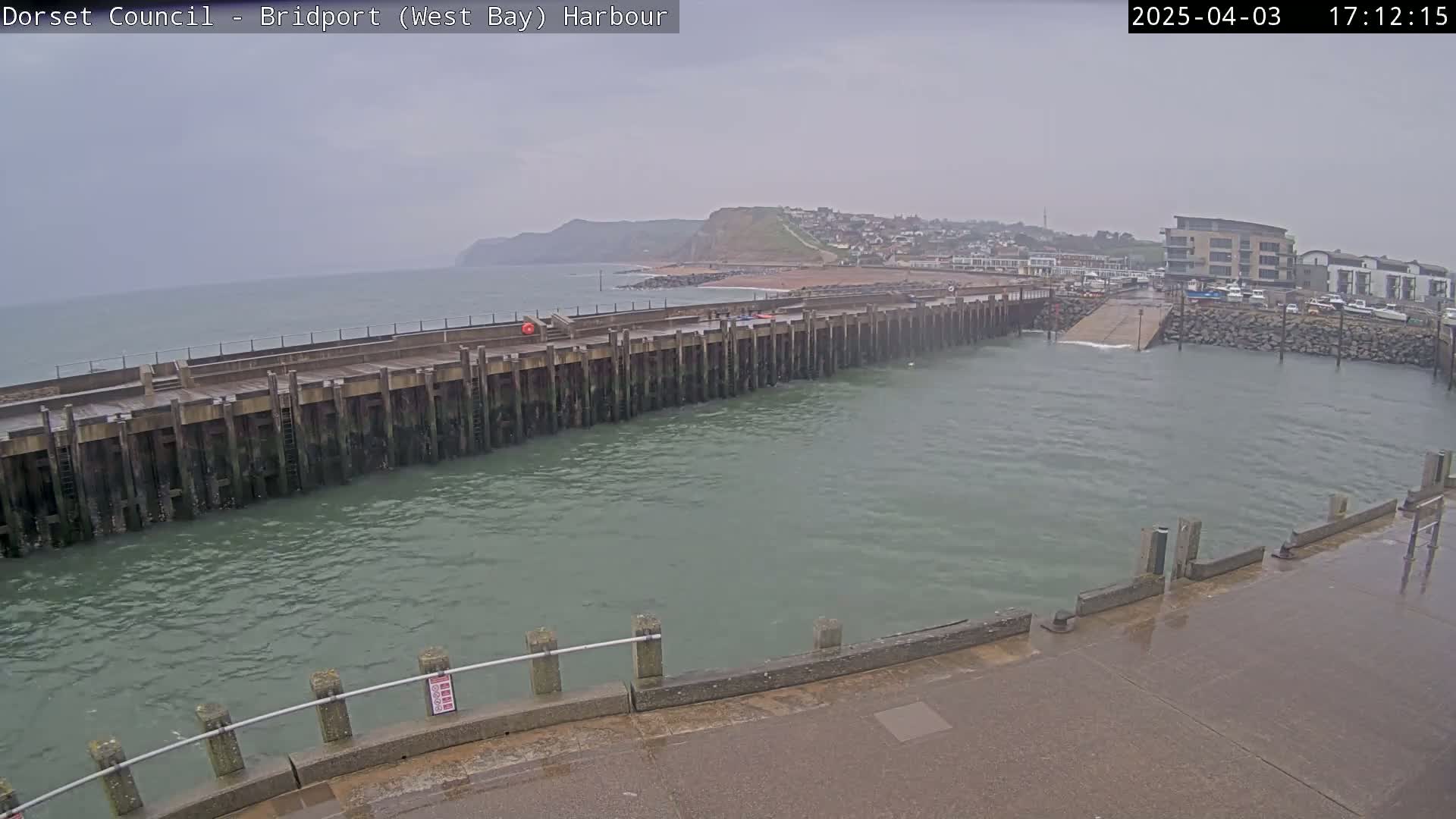 A long, wooden harbor wall extends into a choppy, gray sea under an overcast sky.