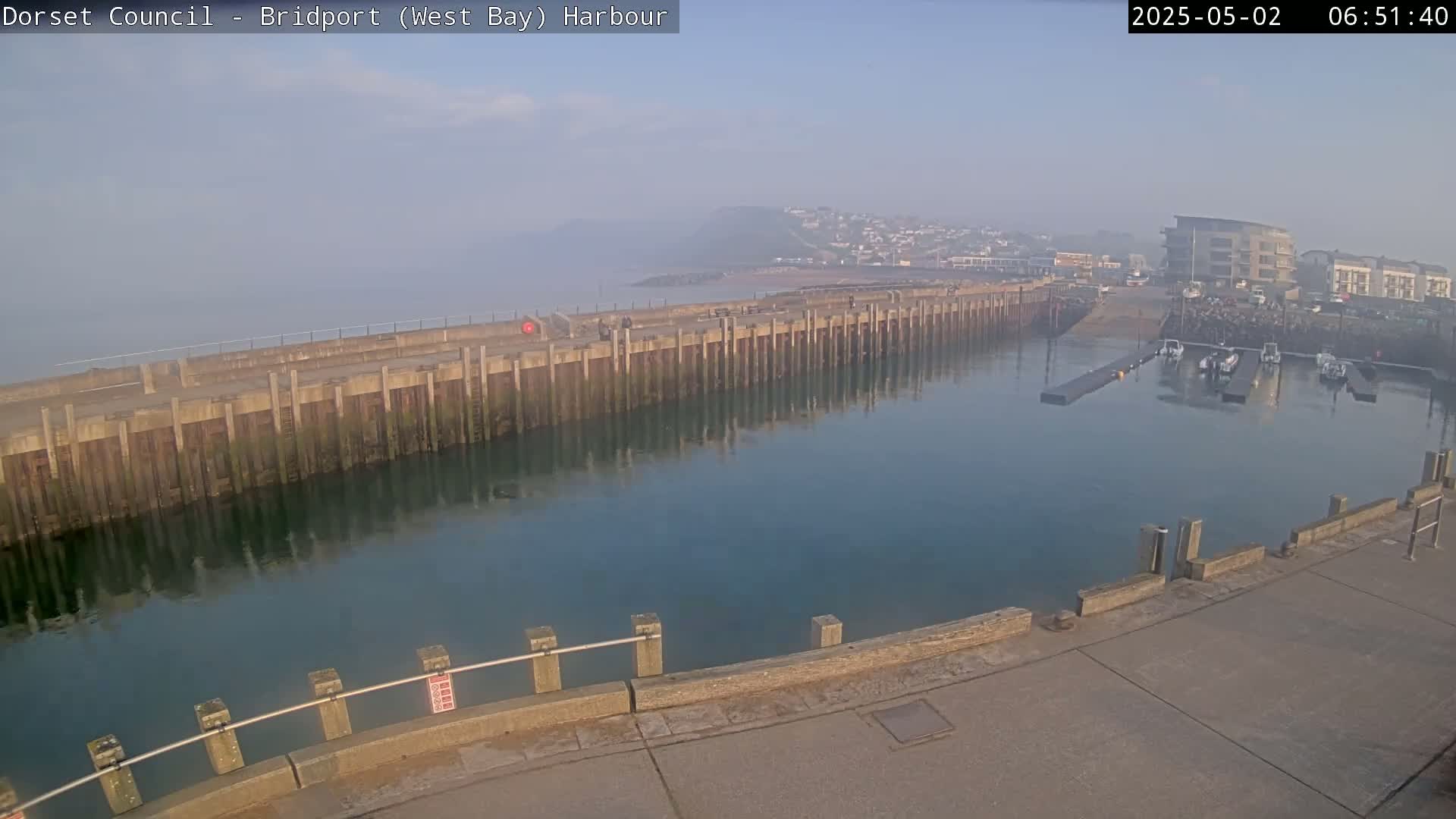 A harbor with calm water, a long pier, several boats docked, and a hazy atmosphere.