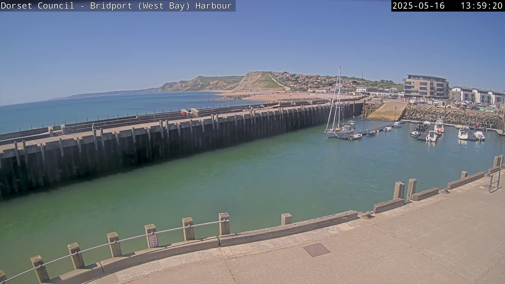 A harbor with several boats docked under a clear blue sky, next to a sandy beach and cliffs.