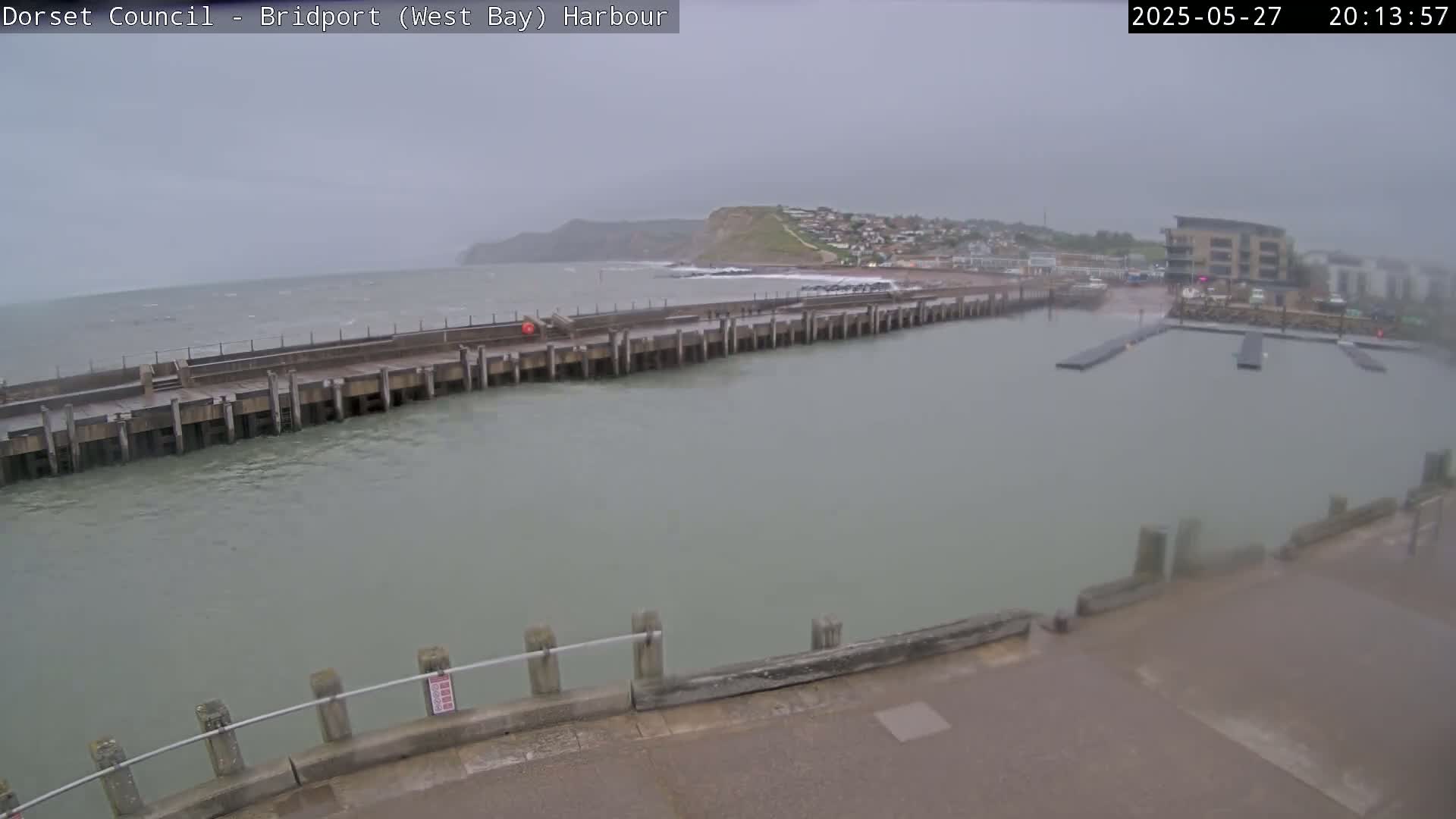 A harbor with a long pier extending into choppy, gray water under an overcast sky.
