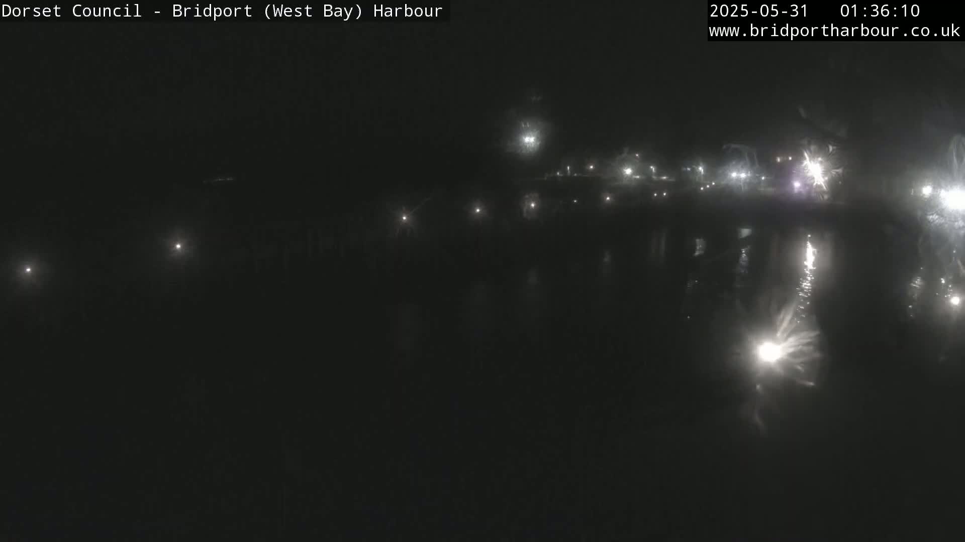 At night, several lights illuminate a dark harbor and its calm, reflective water.
