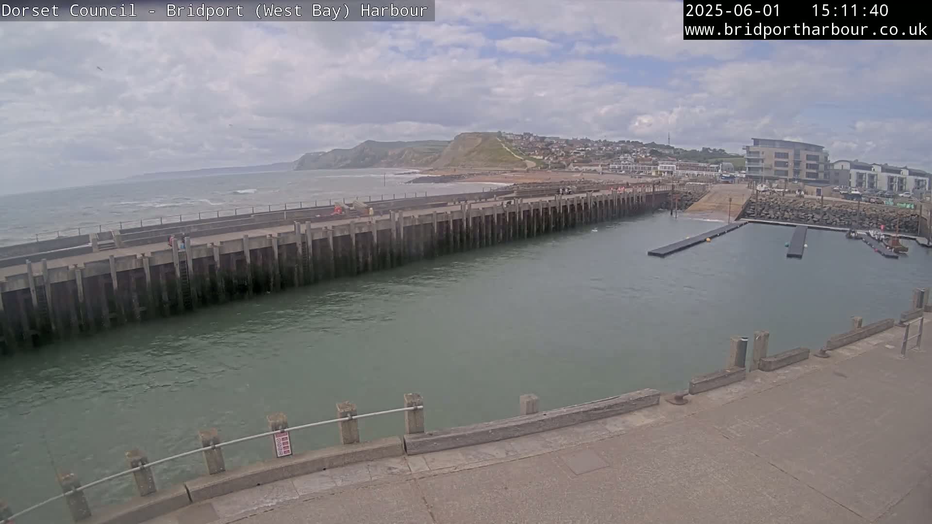 A harbor with a long concrete wall separating it from a choppy sea under a cloudy sky.
