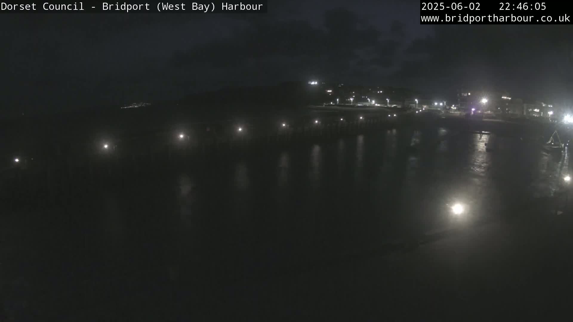 A nighttime, low-light view of a harbor with a pier and faintly visible buildings in the background.