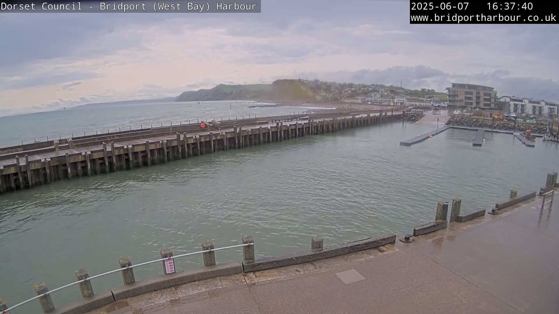 A harbor with a long pier extending into calm, gray water under an overcast sky.