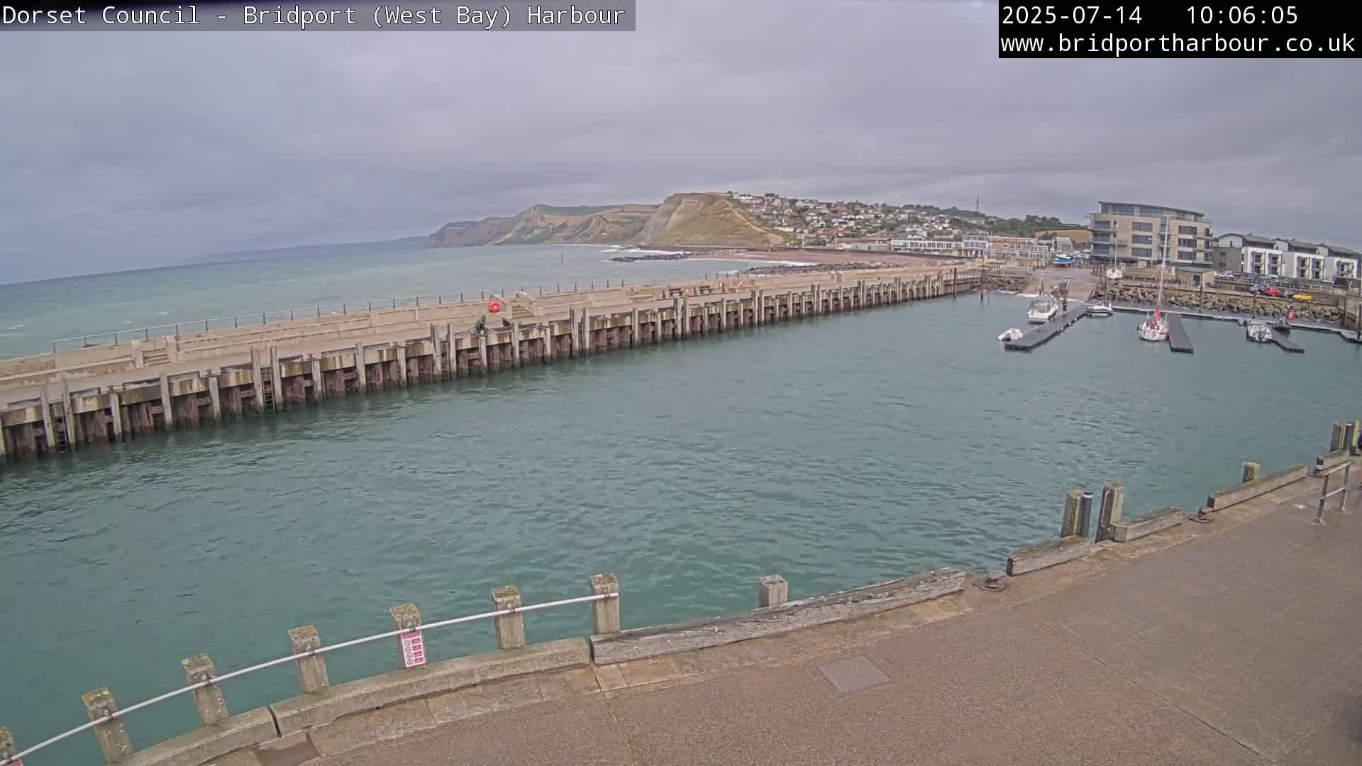 A harbor with a long pier and several boats is seen under an overcast sky.