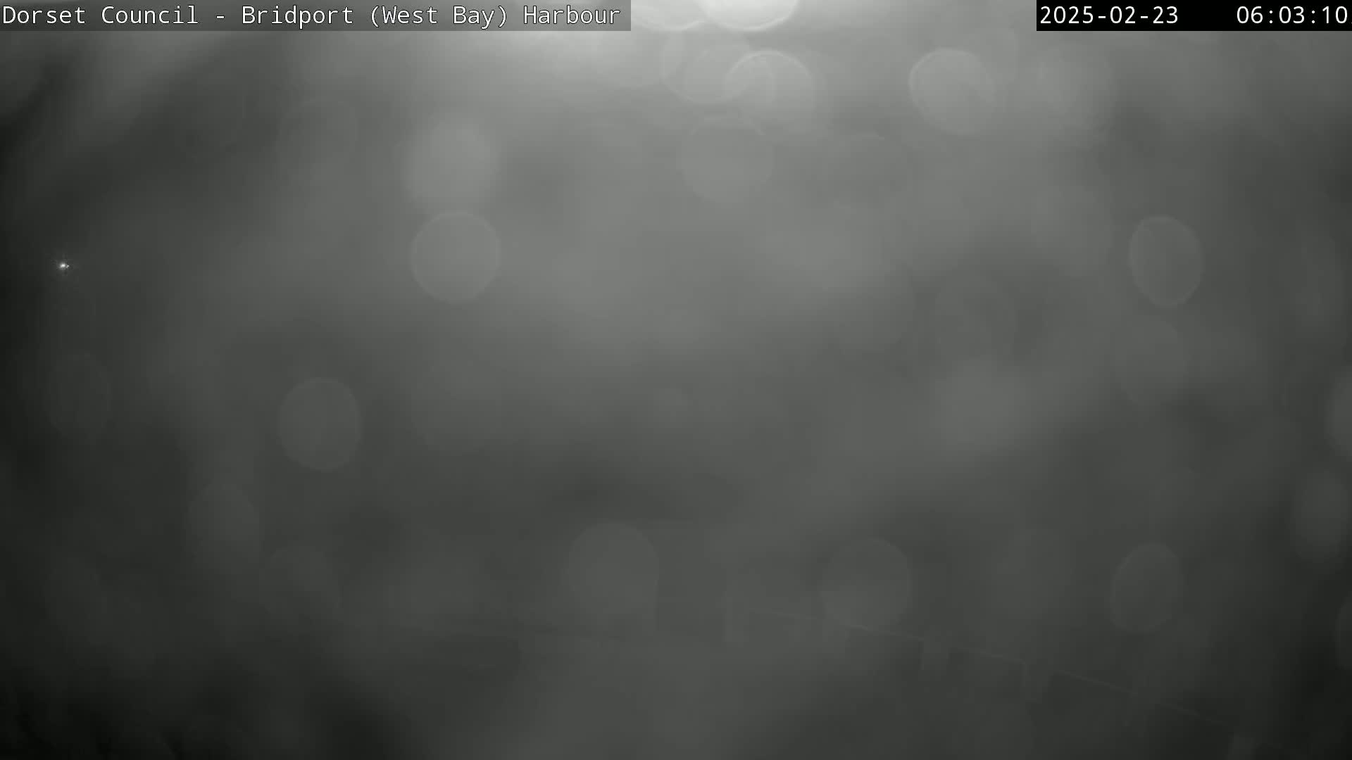A blurry, dark gray image shows out-of-focus light sources resembling raindrops or water droplets in a foggy or misty atmosphere.