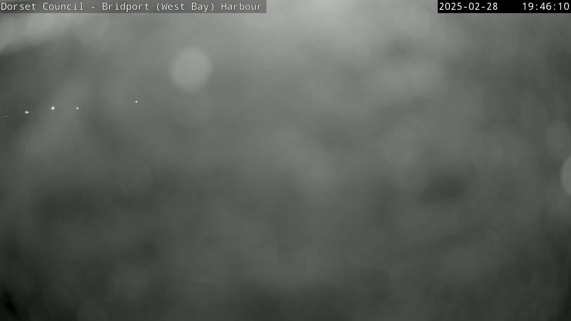 A blurry, dark gray image shows a foggy or hazy scene at night with a few distant lights visible.