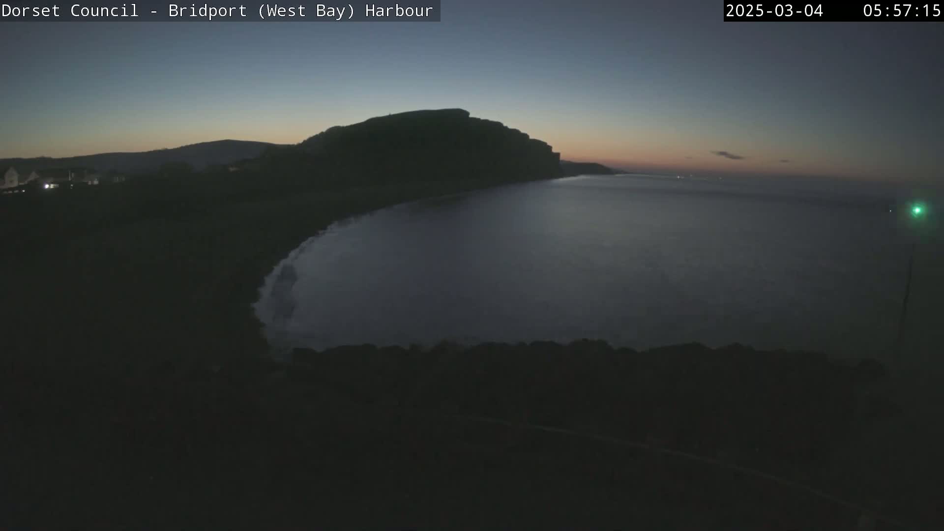 A dark, calm bay is seen at twilight, with a large hill or cliff rising behind it.
