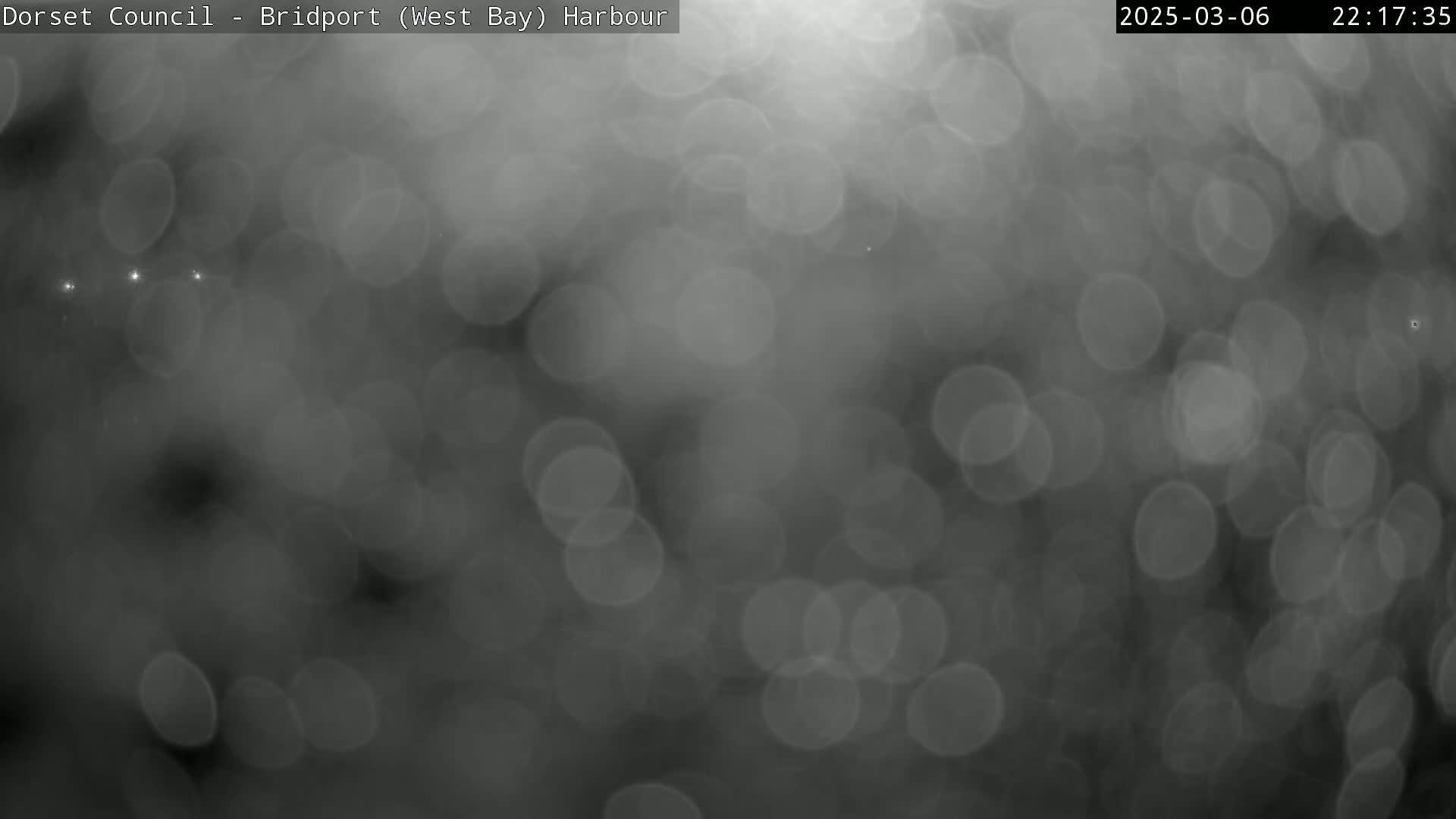 A blurry, grayscale image shows out-of-focus lights resembling raindrops on a window at night.