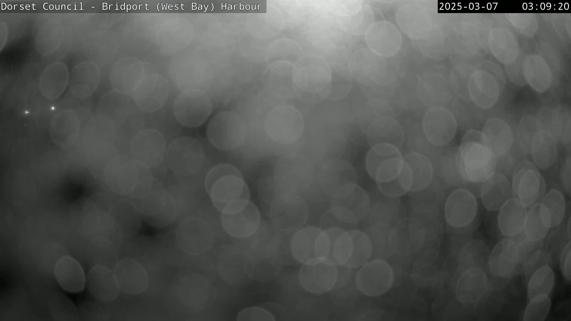 A blurry, out-of-focus image shows a dark grey scene with numerous round bokeh lights suggesting rain or mist.
