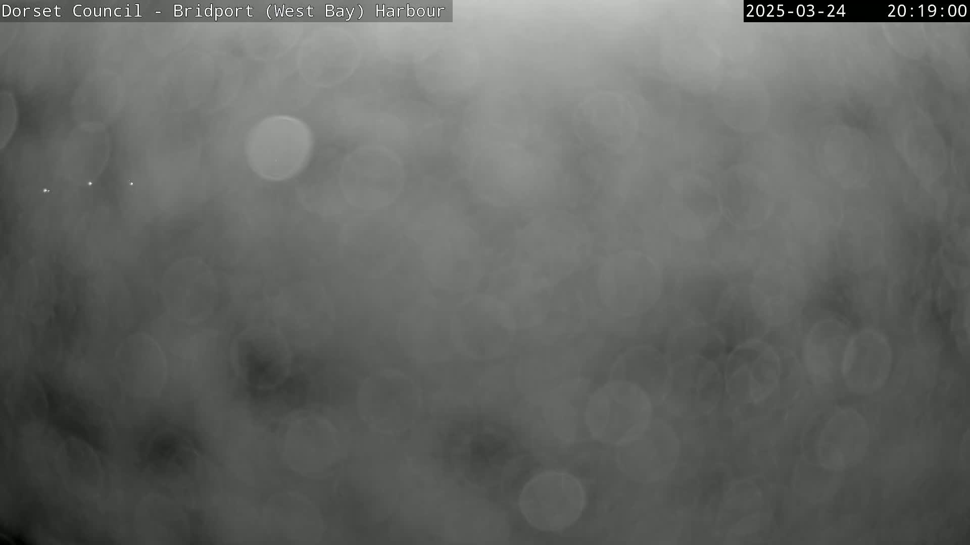 A blurry, dark gray image shows a heavily overcast or foggy scene with numerous out-of-focus light circles.