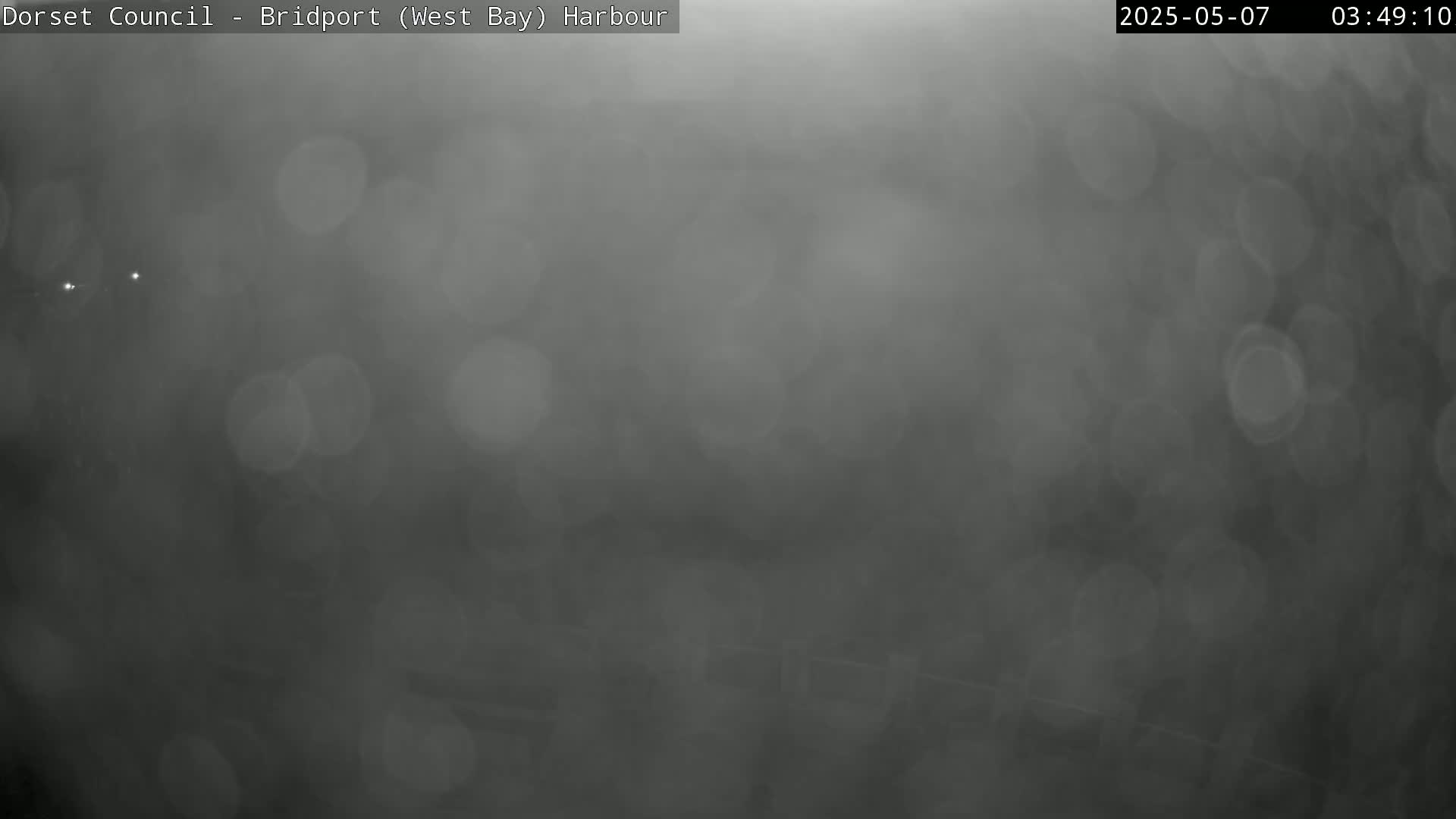 A blurry, dark gray image shows a foggy or hazy outdoor scene with indistinct shapes and bright spots of light.