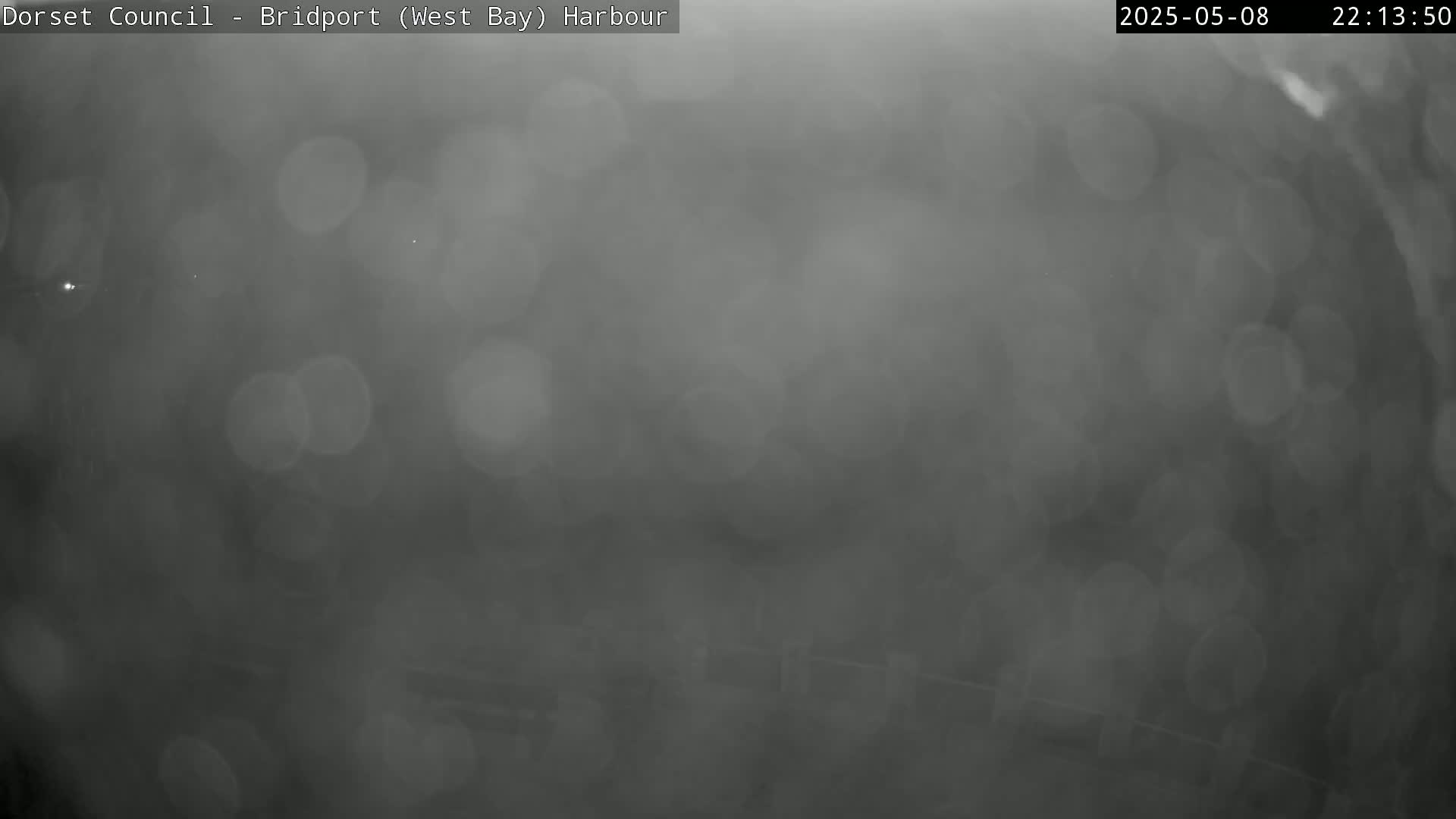 A blurry, dark gray image shows out-of-focus light sources in rainy conditions.