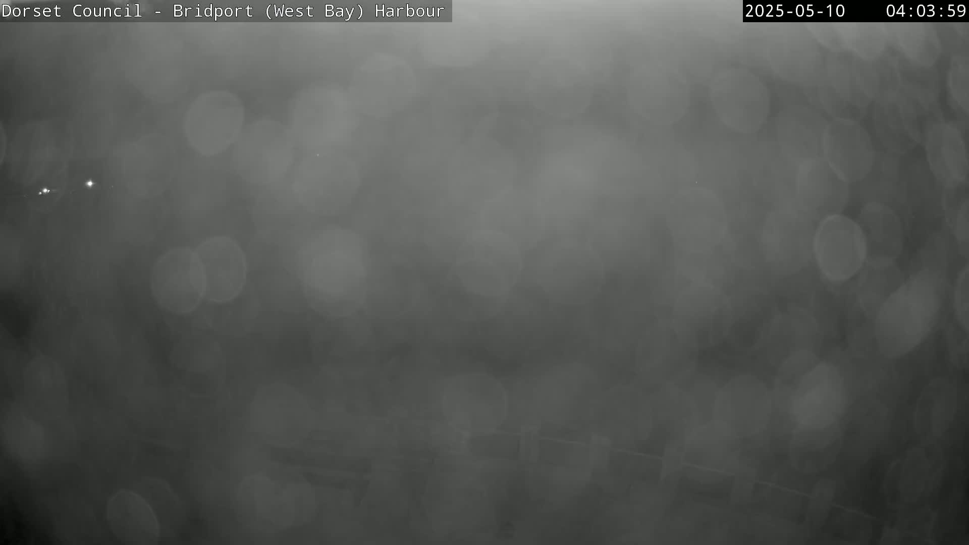A blurry, dark gray image shows a foggy or hazy harbor scene at night.