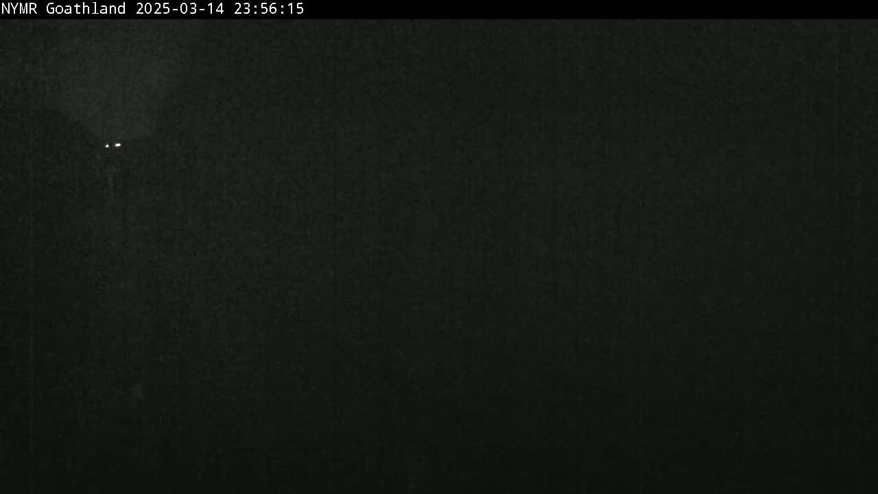 A dark, nighttime image shows a pair of distant headlights on a dark road.