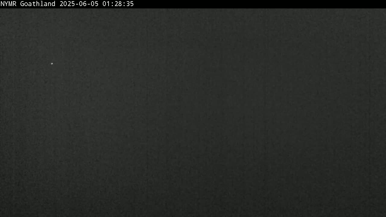 A dark, nighttime image shows a mostly featureless, dark gray or black sky with one small, faint light source.