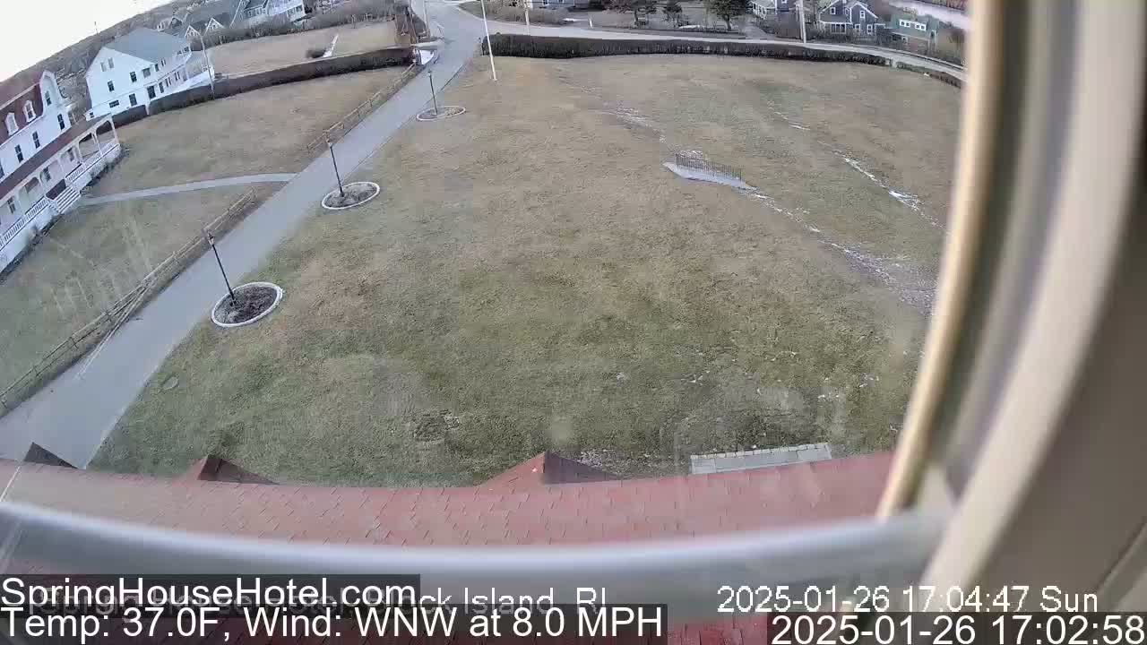 A view from a window shows a grassy area with walkways and buildings in the background, under sunny conditions with a temperature of 37°F and a west-northwest wind at 8.0 mph.