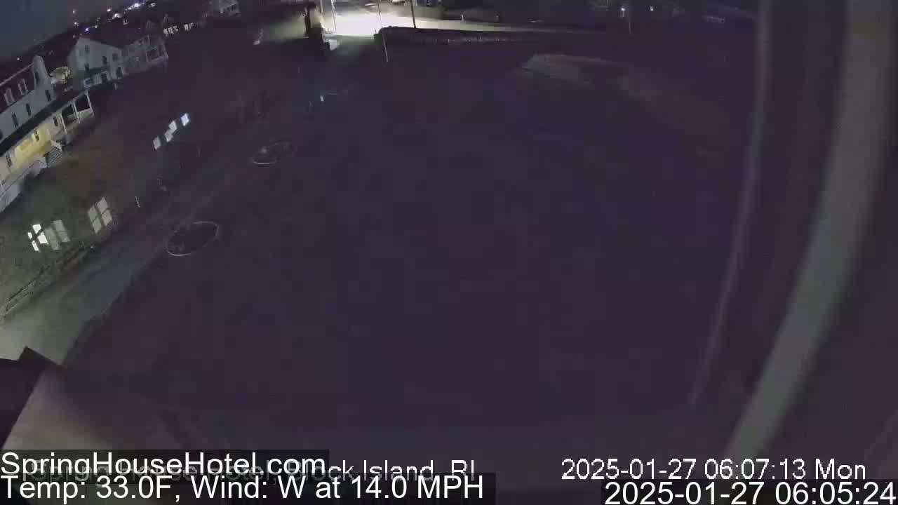 Here's a description of the image: A nighttime, high-angle view of a street scene with buildings, a parking lot, and a westerly wind at 14 miles per hour and a temperature of 33 degrees Fahrenheit.