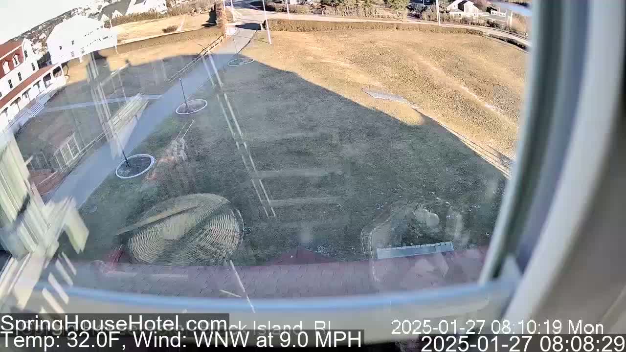 A view from a window shows a mostly barren, brown lawn with some landscaping and a building in the background, on a 32°F day with a 9.0 mph wind from the west-northwest.