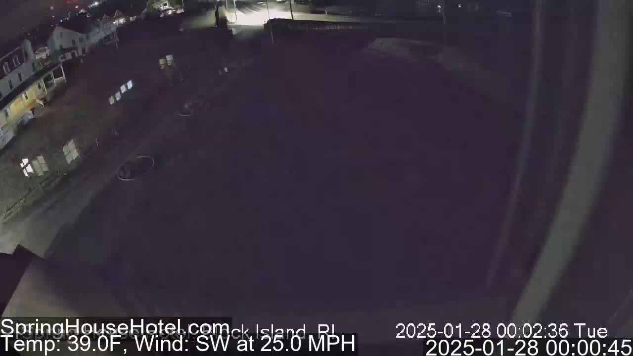 A nighttime, dark overhead view of a mostly empty parking lot and street near buildings, under a dark sky with a southwest wind at 25 mph and a temperature of 39°F.