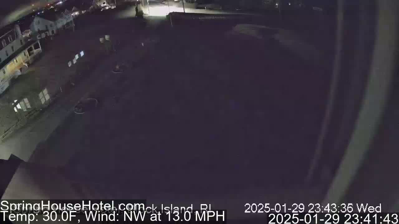 A nighttime, outdoor view of a mostly empty parking lot next to buildings, with a northwest wind at 13 miles per hour and a temperature of 30 degrees Fahrenheit.