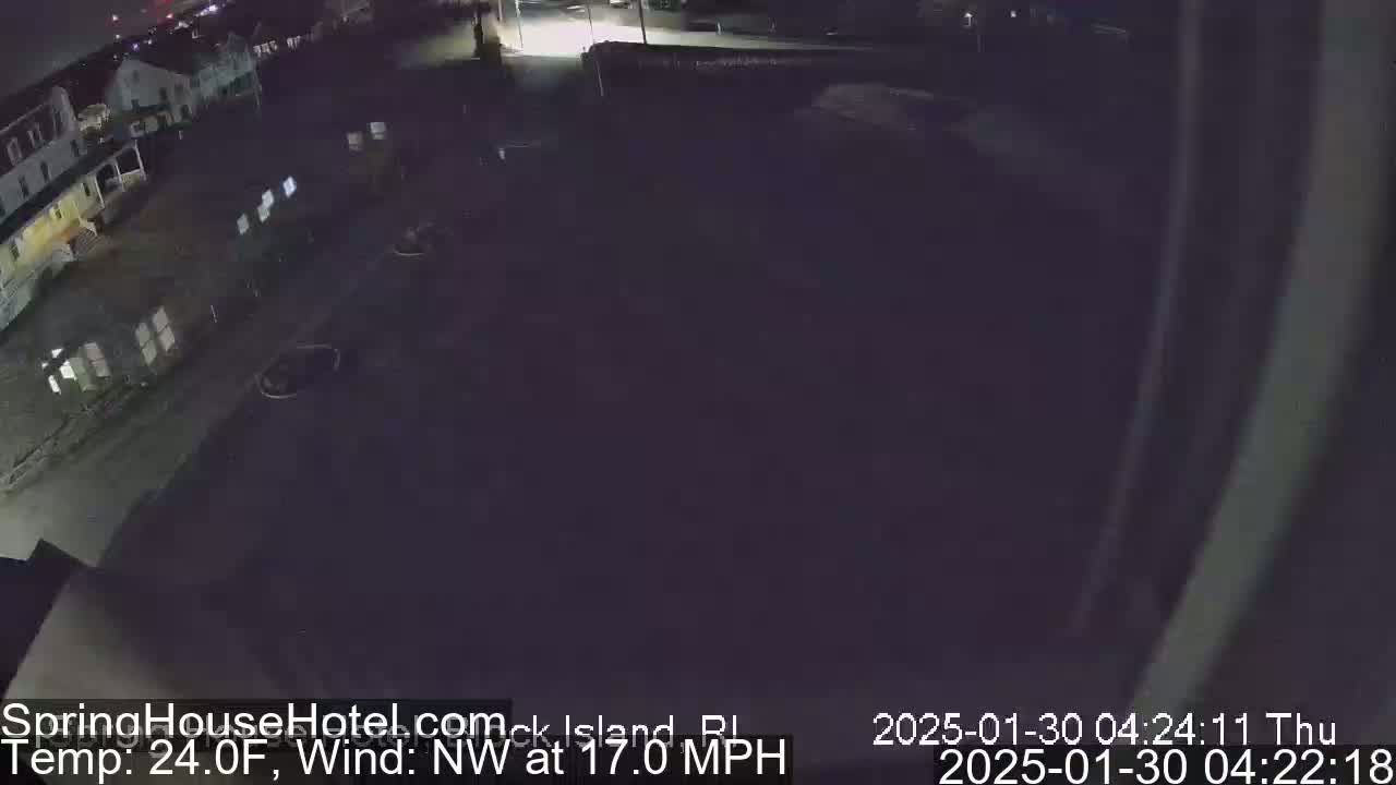 A nighttime, overhead view of a mostly empty parking lot next to a building, with a northwest wind at 17 mph and a temperature of 24 degrees Fahrenheit.