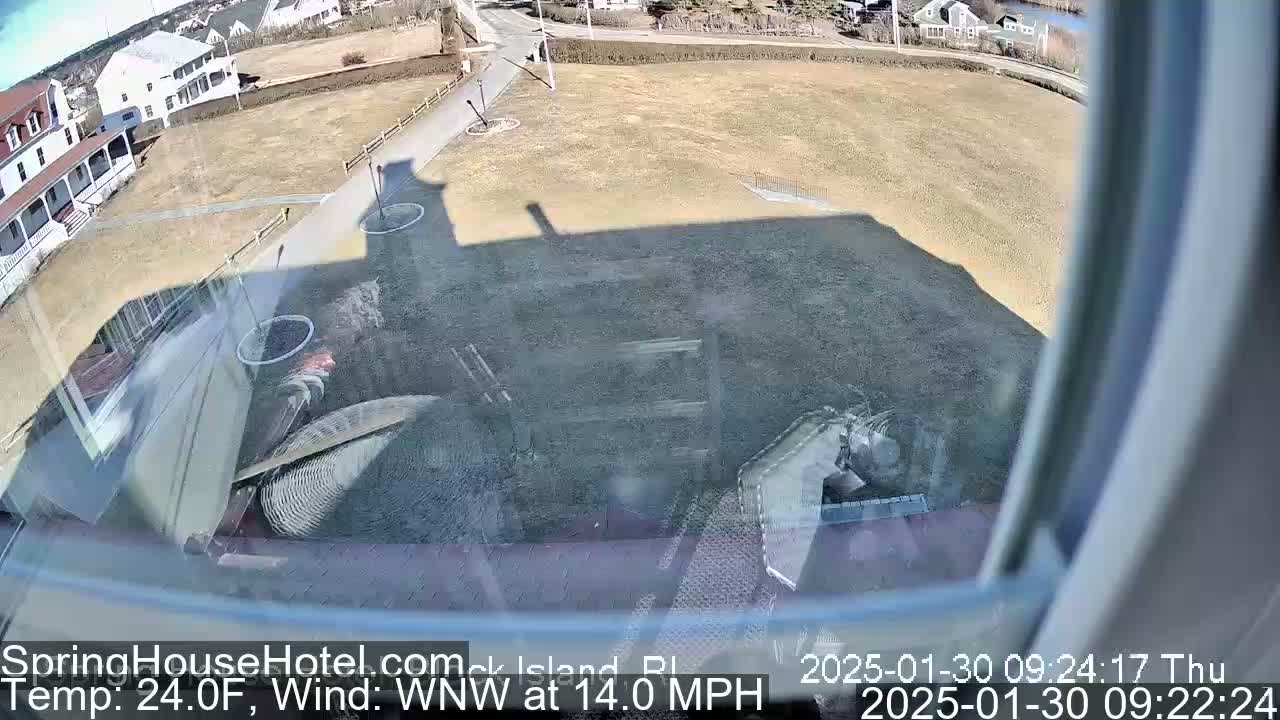 A mostly sunny view from a window shows a brown, grassy area with a building and a road, with a wind of 14 mph from the west-northwest and a temperature of 24 degrees Fahrenheit.