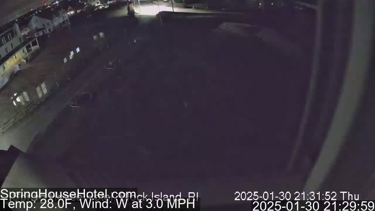 A nighttime, high-angle view of a dark parking lot and street with several buildings in the background under a clear sky, with a light westerly wind at 3 mph and a temperature of 28°F.