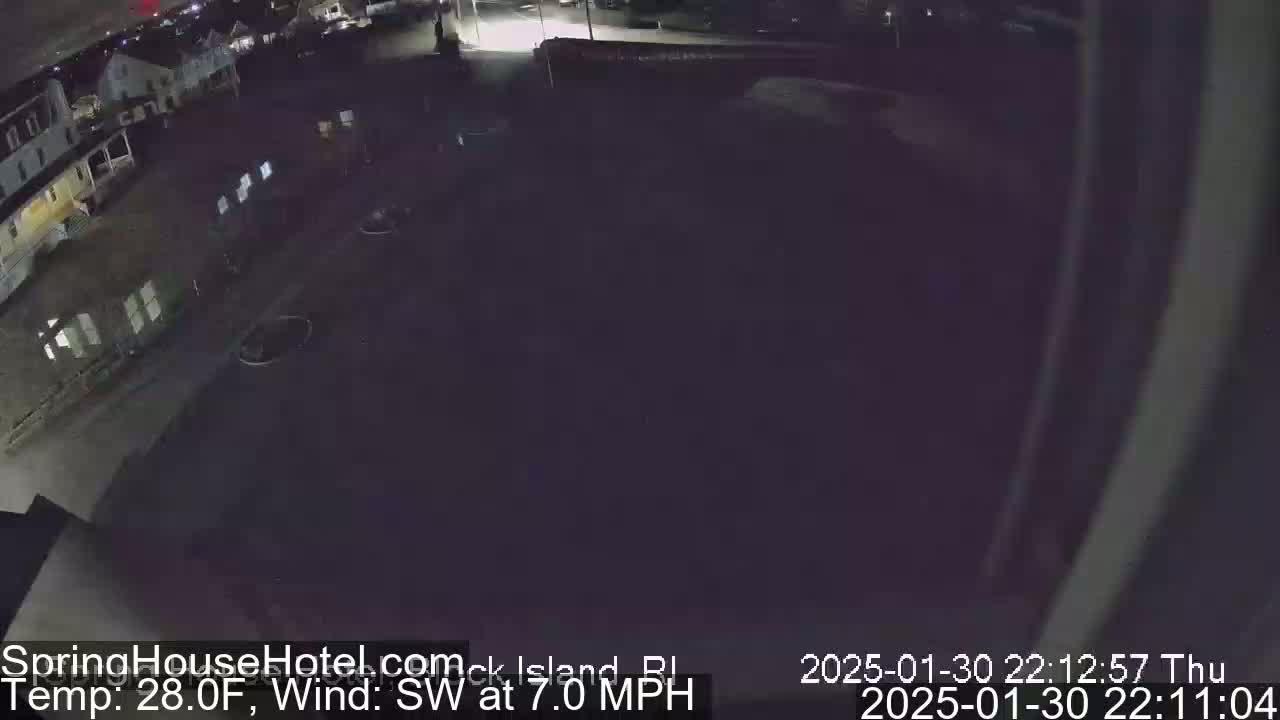 A nighttime, overhead view of a mostly empty parking lot and street in front of a building, with a southwest wind at 7 mph and a temperature of 28 degrees Fahrenheit.