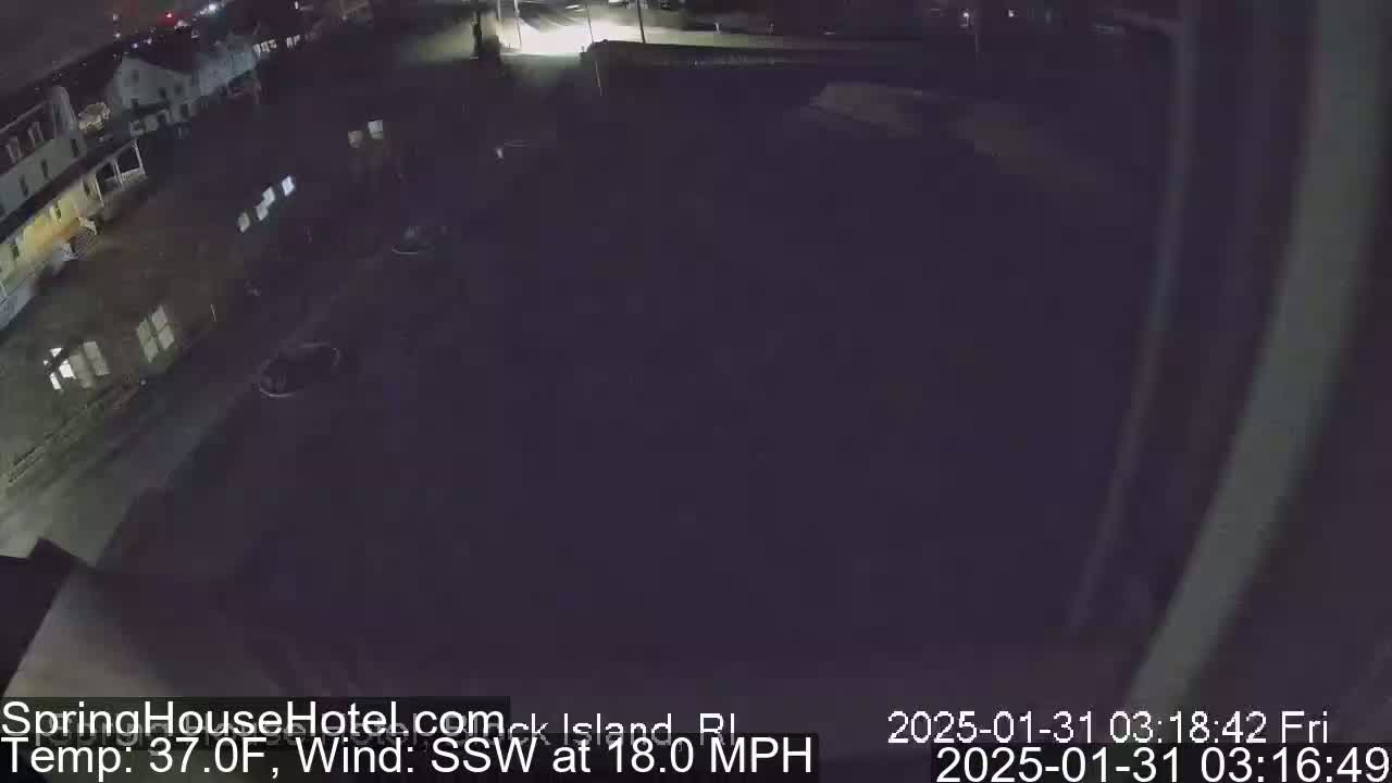 A nighttime, low-light view of a street and buildings under a dark sky with an 18 mph wind from the south-southwest.