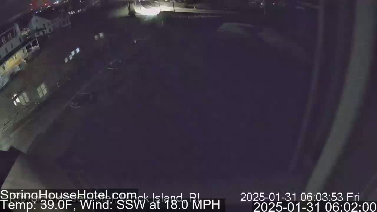 A nighttime, outdoor view of a parking lot and buildings under a dark sky with a strong south-southwesterly wind at 18 mph and a temperature of 39°F.