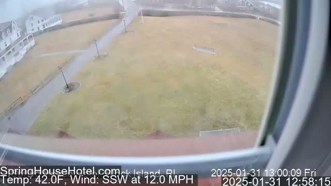 A wide shot from a window shows a grassy area with walkways and lampposts, under an overcast sky with light precipitation.