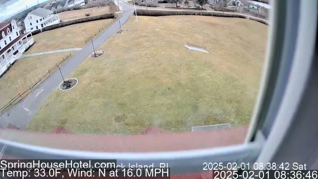 A view from a window shows a large grassy area with a paved pathway, some landscaping, and buildings in the background, all under windy, 33-degree Fahrenheit weather.