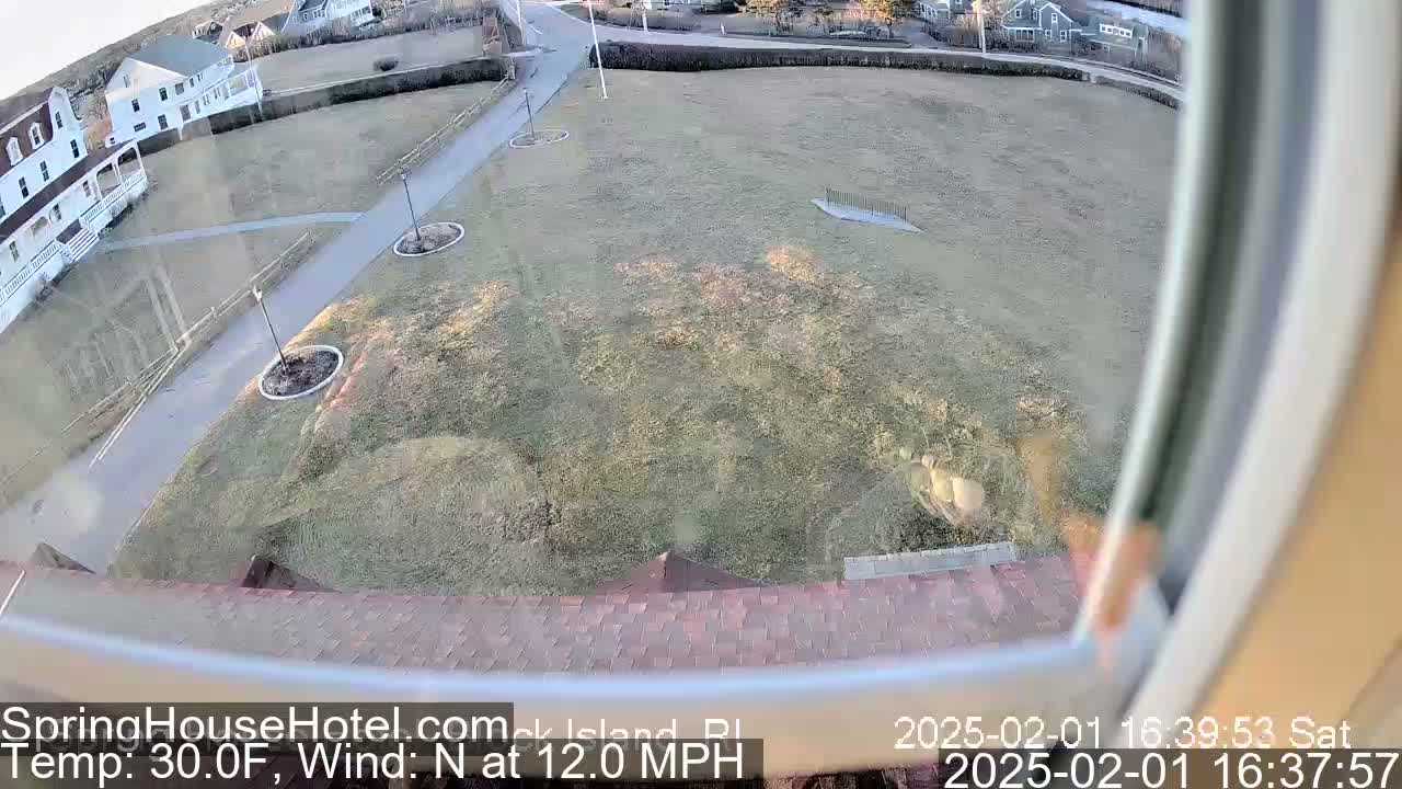 A high-angle, outdoor view shows a grassy area with a building and a paved path, under sunny skies and a north wind of 12 mph at 30°F.