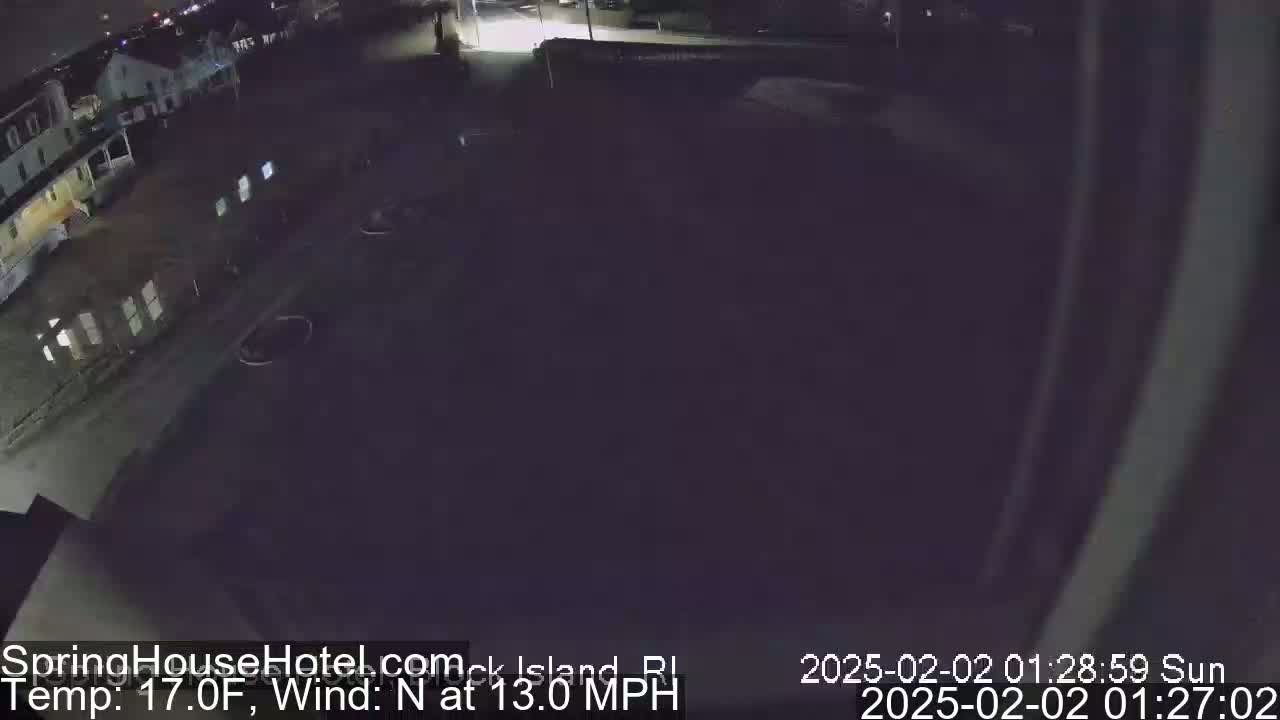 A nighttime, low-angle view of a mostly empty parking lot next to a building, under a dark sky with a north wind at 13 mph and a temperature of 17°F.