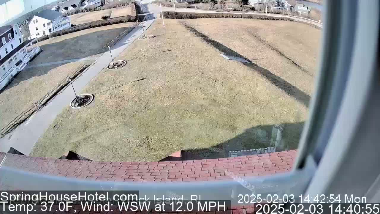 A view from a window shows a grassy area with walkways, landscaping, and buildings in the background, under windy, 37°F weather.