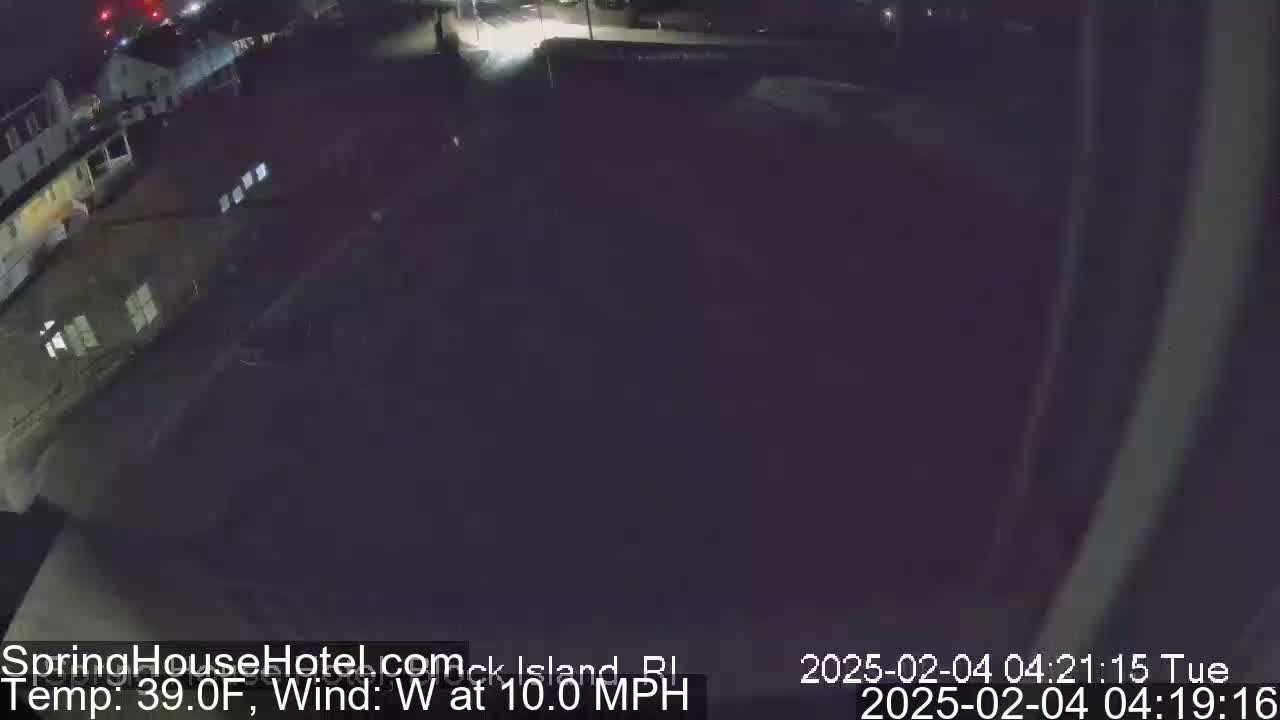 A nighttime, overhead view of a dark, mostly empty parking lot and buildings with a west wind blowing at 10 mph and a temperature of 39°F.
