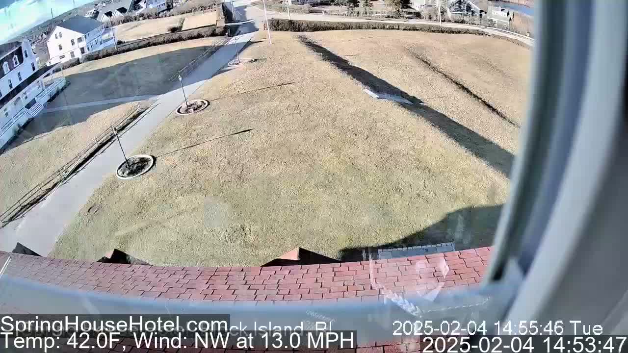 A high-angle view shows a brown grassy area with a paved pathway and buildings in the background under a sunny sky with a northwest wind of 13 mph and a temperature of 42°F.