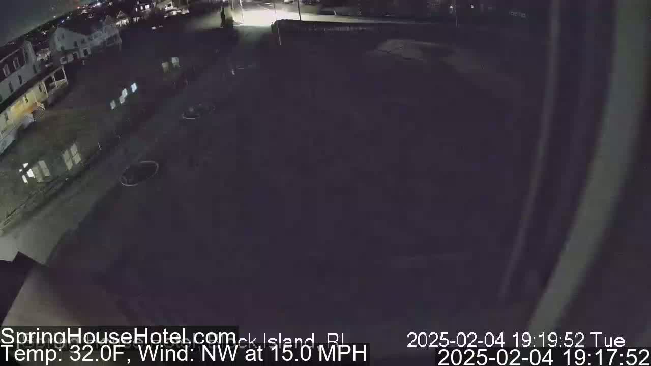 A nighttime, outdoor view of a mostly empty parking lot and street next to a building, with a northwest wind at 15 mph and a temperature of 32 degrees Fahrenheit.