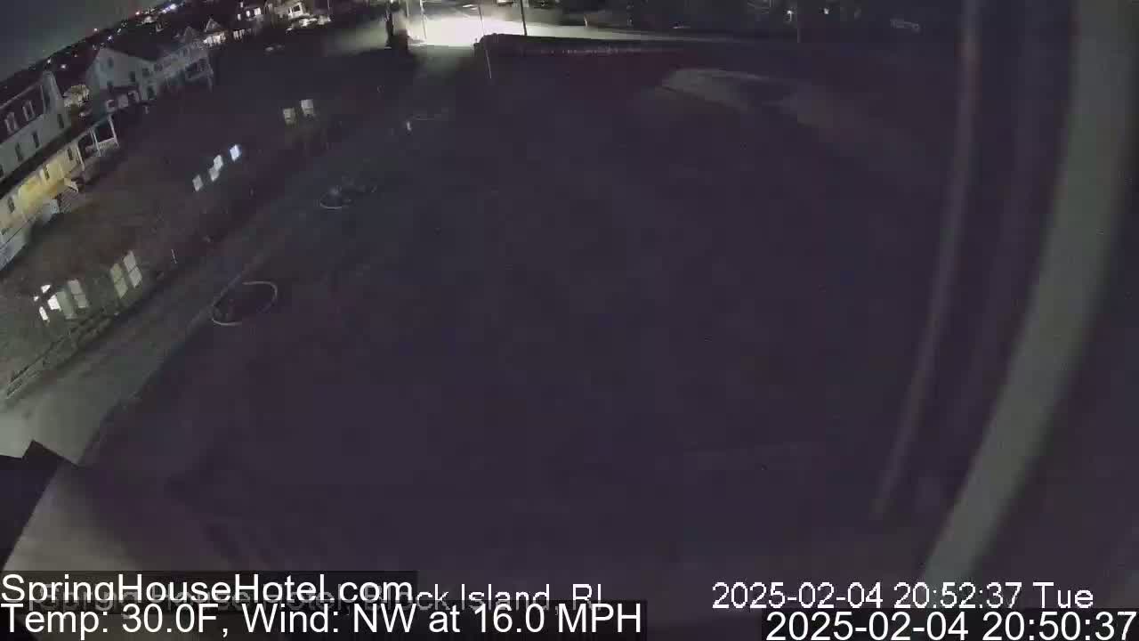 A nighttime, high-angle view of a mostly empty parking lot next to a building complex under a dark sky, with a northwest wind blowing at 16 mph and a temperature of 30°F.