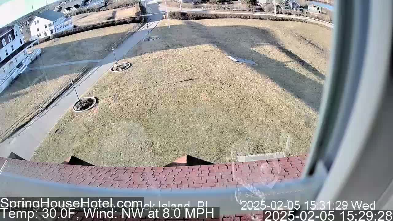 A view from a window shows a brown grassy area with a paved walkway, buildings in the distance, and a northwest wind at 8 mph with a temperature of 30 degrees Fahrenheit.