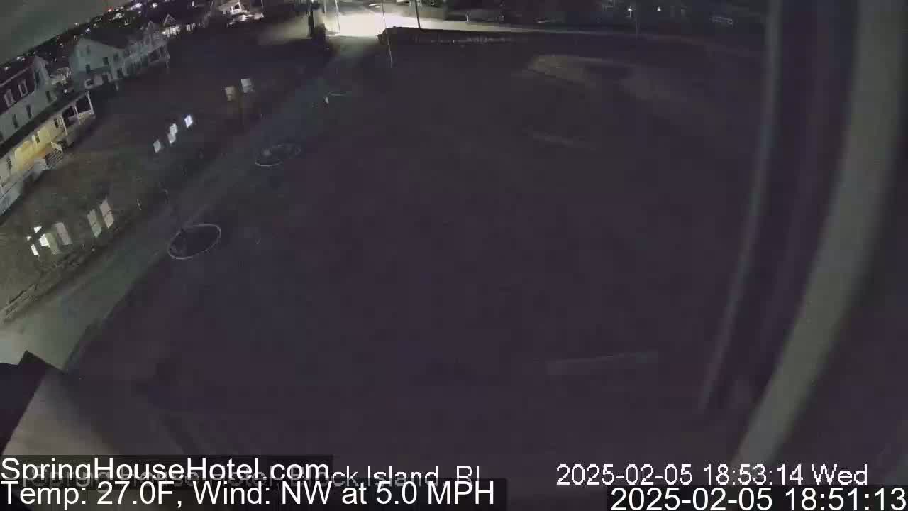 A nighttime, wide shot of a mostly empty parking lot next to a residential area with a northwest wind at 5.0 mph and a temperature of 27 degrees Fahrenheit.