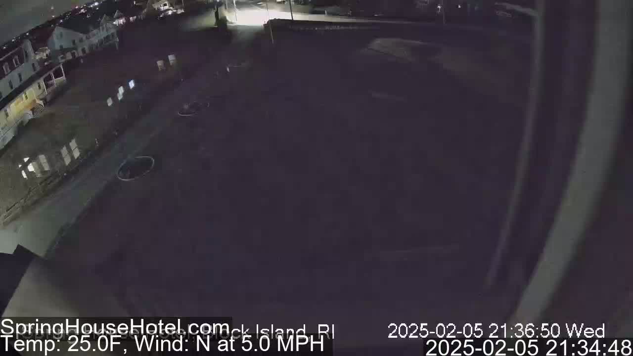A nighttime, high-angle view of a mostly empty parking lot next to a building, with a 25°F temperature and a 5 mph north wind.